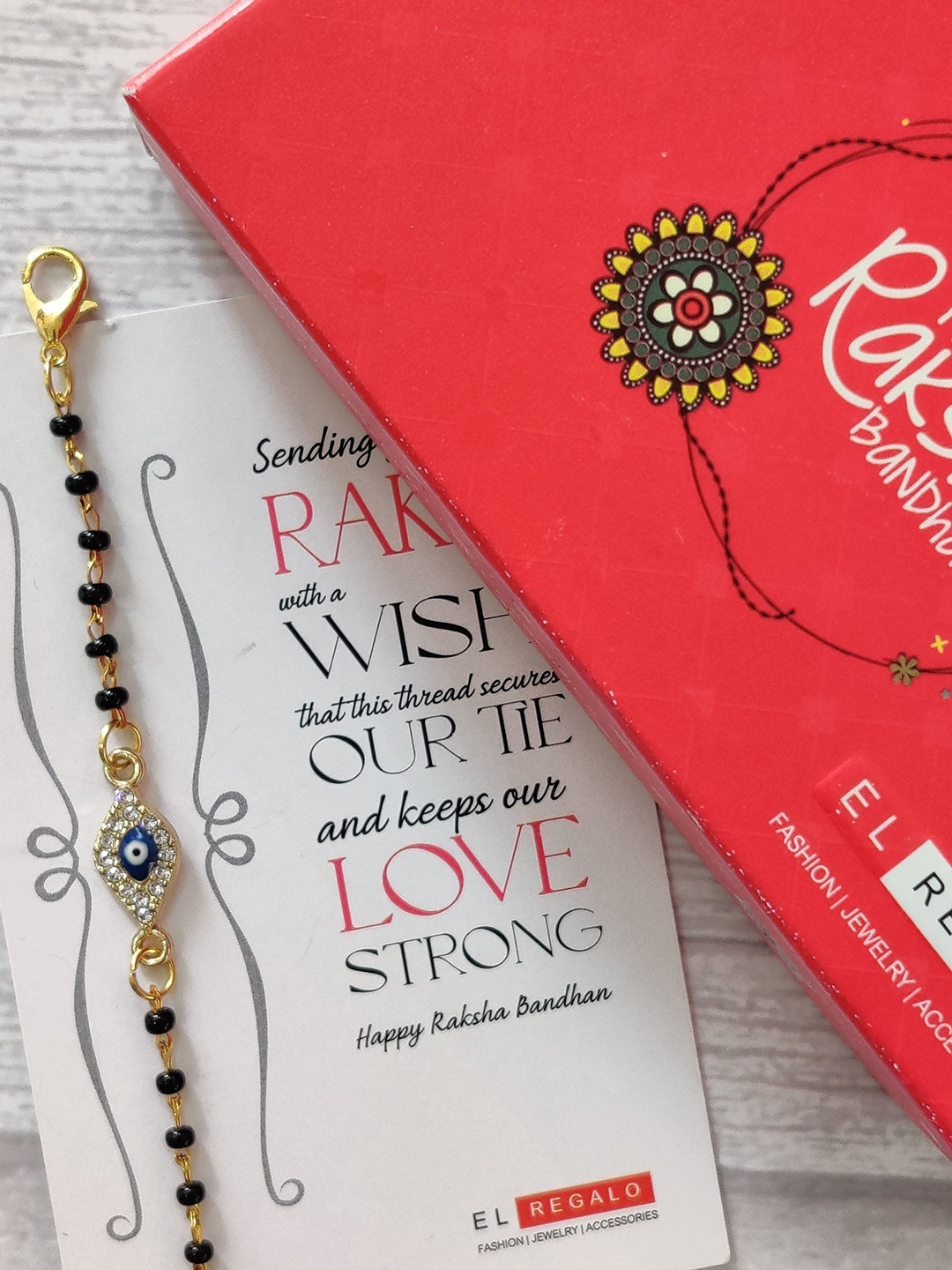 EL REGALO Kids Gold-Toned Nazaria Rakhi Combo with Greeting Card & Roli Chawal Shagun
EL REGALO Kids Gold-Toned Nazaria Rakhi Combo with Greeting Card & Roli Chawal Shagun