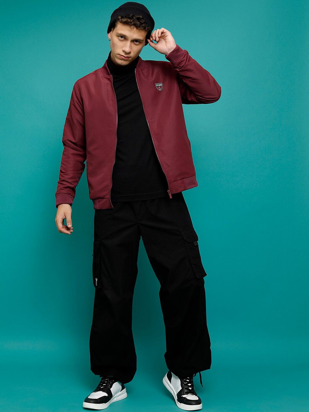 Maroon bomber jacket worn over a black top with loose black cargo trousers and high-top sneakers