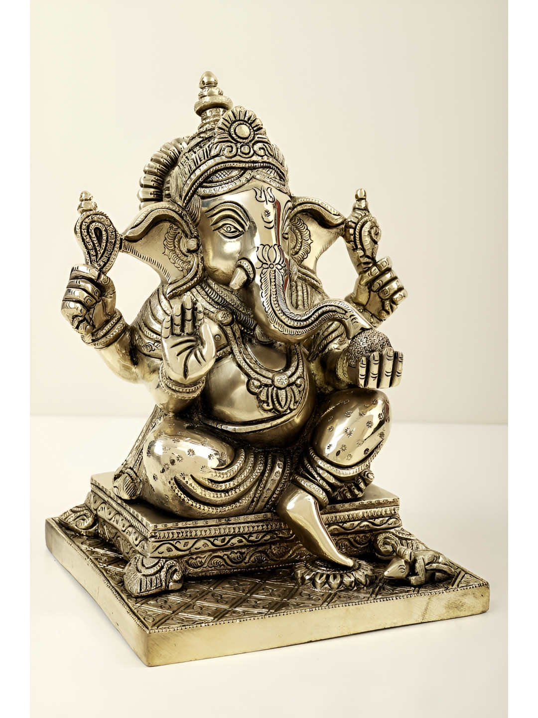 Exotic India Lord Ganesha Seated On Pedestal And Eating Modak Gold Brass Metallic Prayer Room Medium Showpiece - 9.5 Inches
