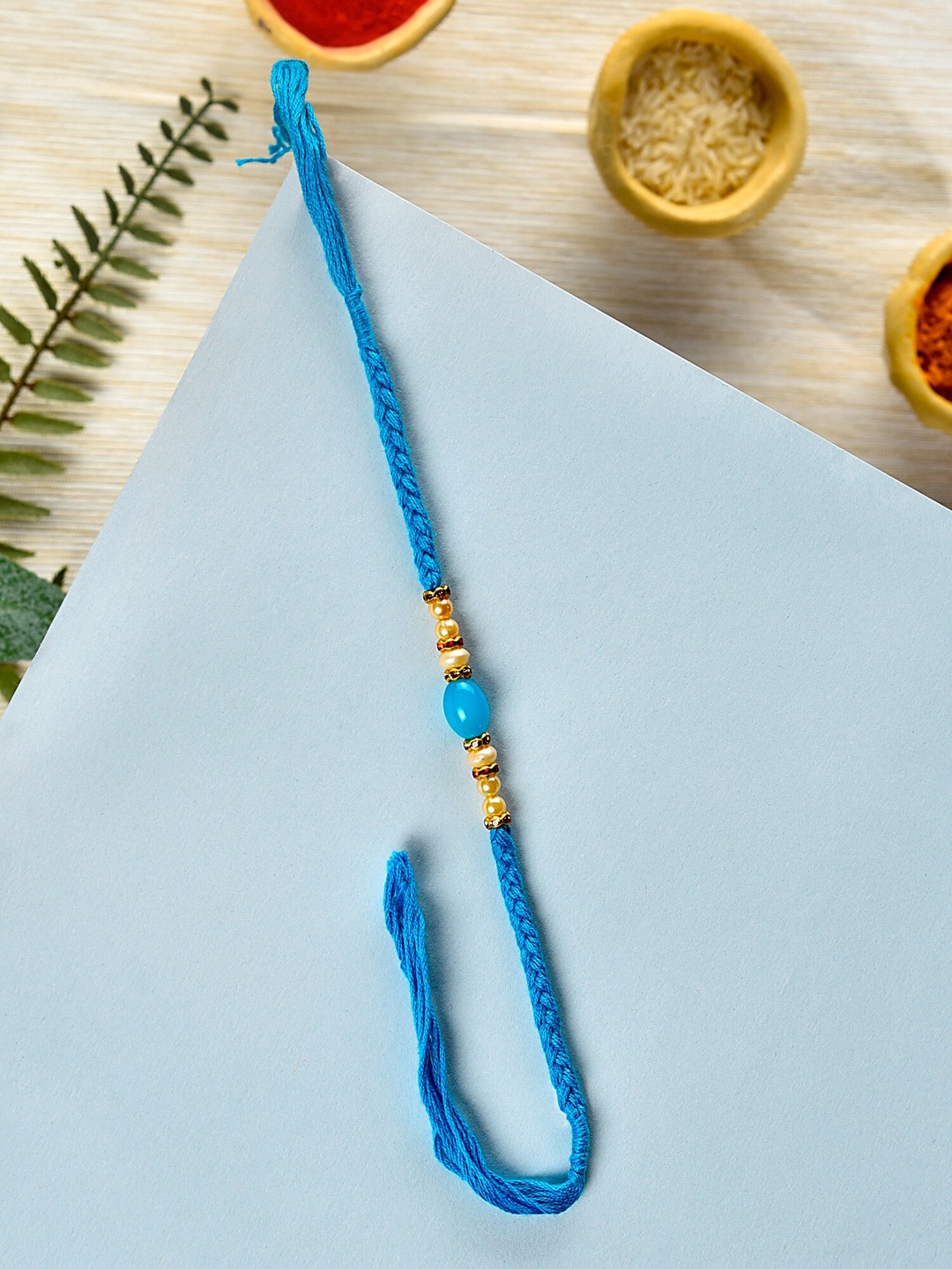 

Zaveri Pearls Blue Bead Embellished Rakhi With Chawal Roli