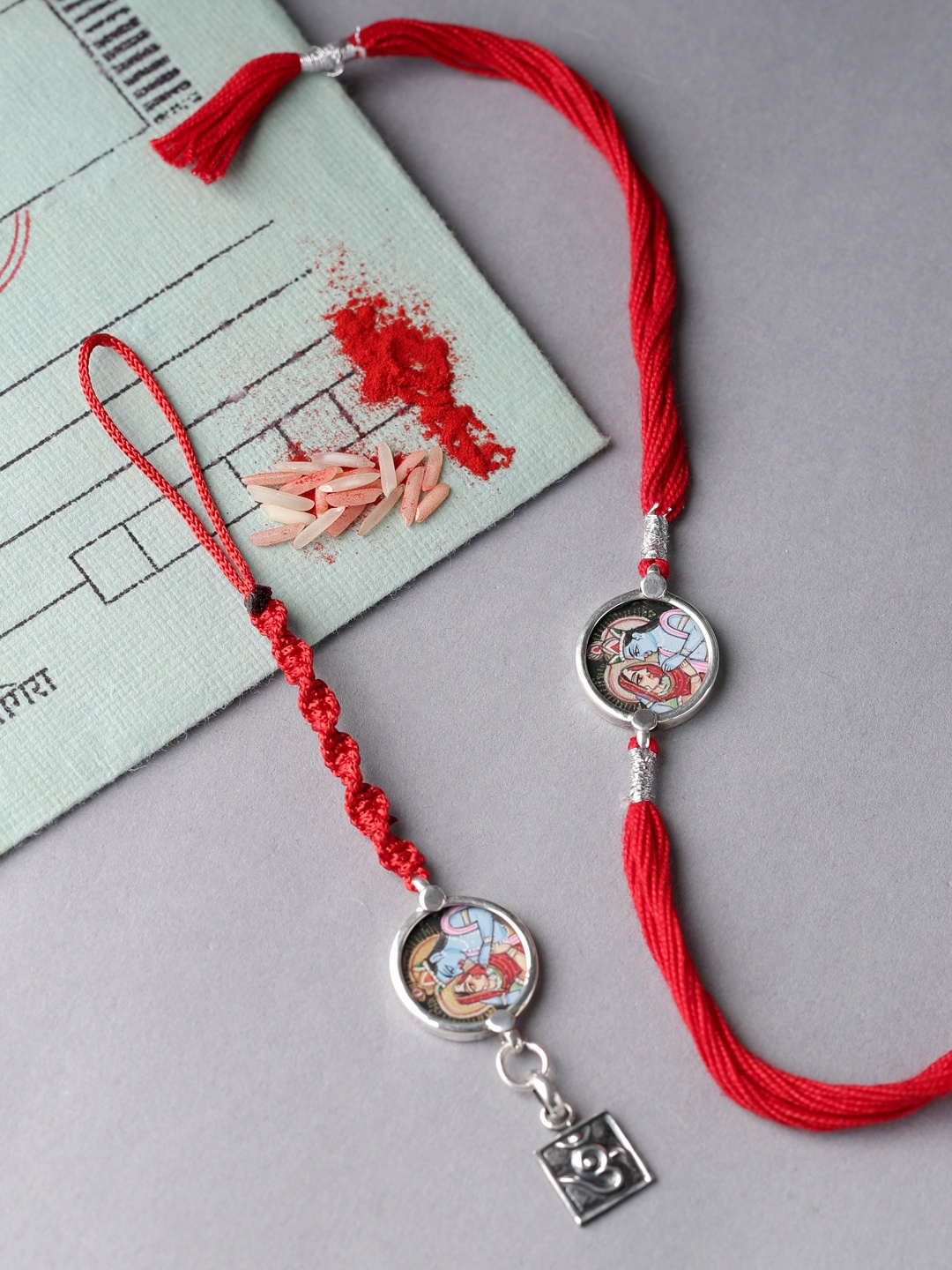 

ADORN by Nikita Ladiwala Silver-Toned & Red Radha Krishna Rakhi
