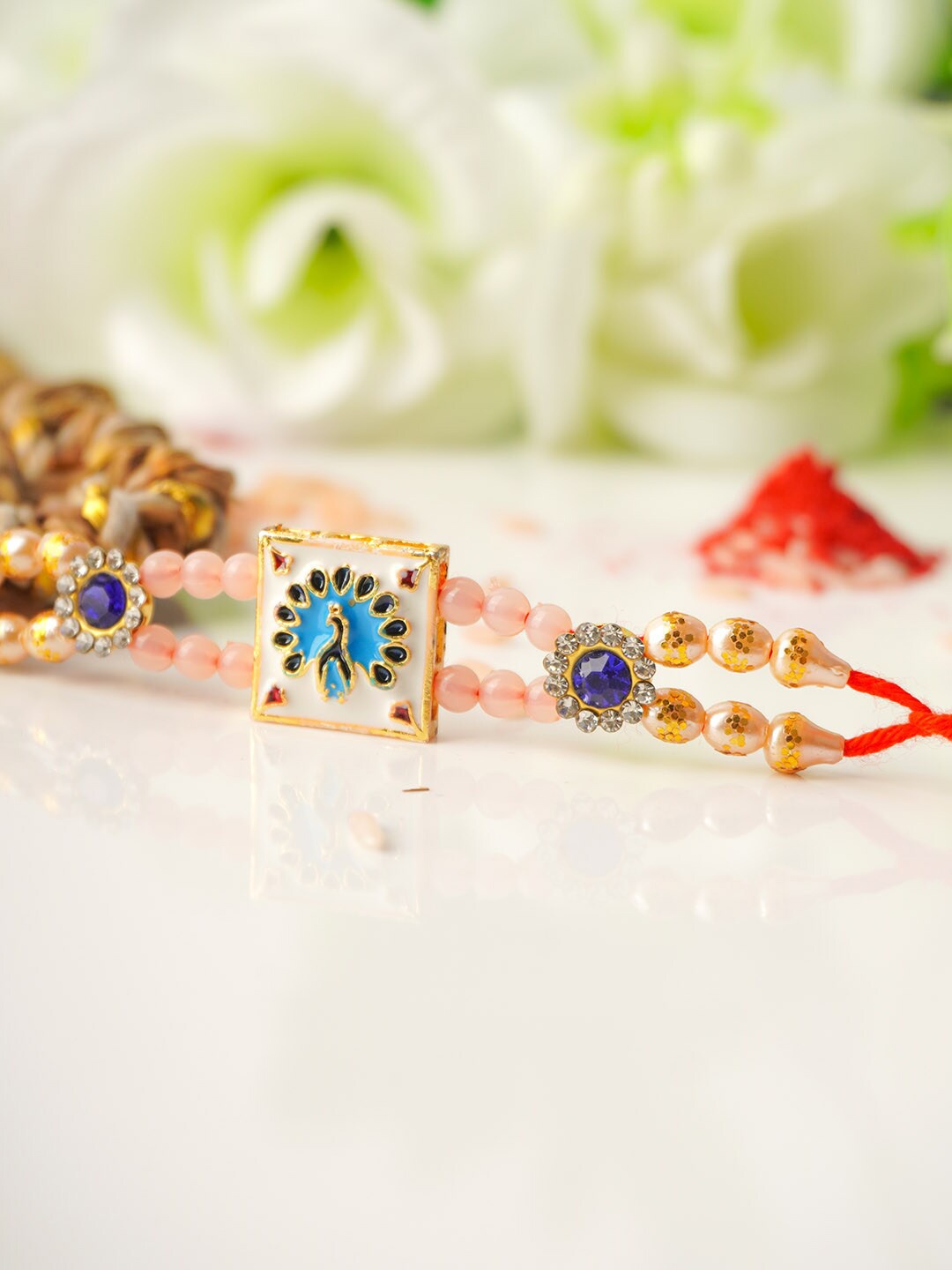 

Urmika Men Gold-Toned White & Blue Stone Studded Peacock Motif Rakhi With Roli Chawal