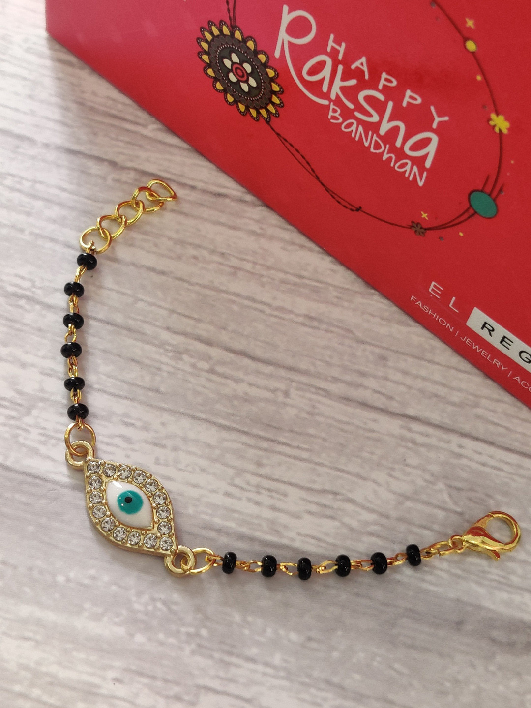 

EL REGALO Kids Gold-Toned Nazaria Rakhi Combo with Greeting Card & Roli Chawal Shagun