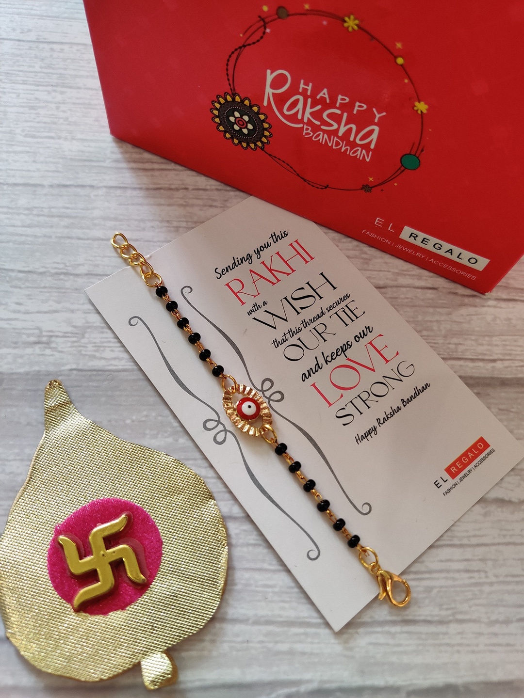 

EL REGALO Kids Gold-Toned Nazaria Rakhi Combo with Greeting Card & Roli Chawal Shagun