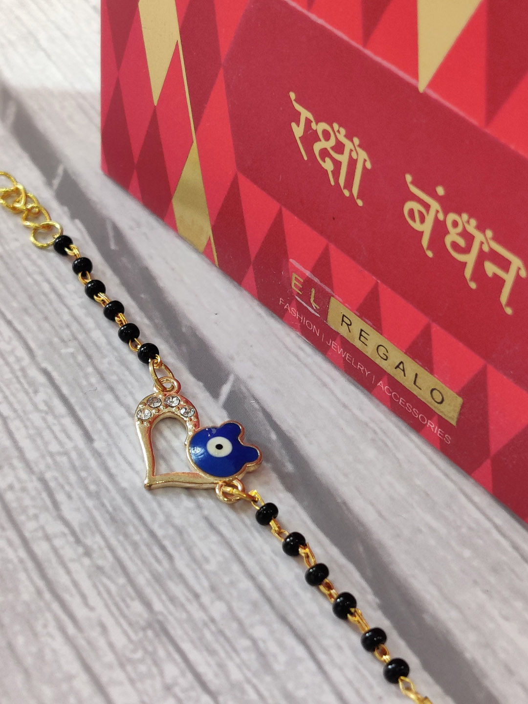 

EL REGALO Gold Coloured Blue Evil Eye Rakhi With Roli Chawal Rakhi Card