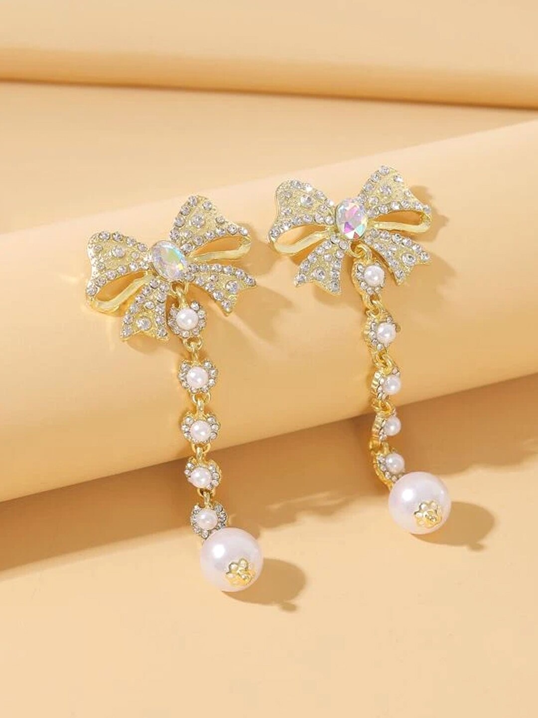 

Yellow Chimes Gold-Toned Crystal & Pearl Studded Bow Knot Shaped Dangle Earrings