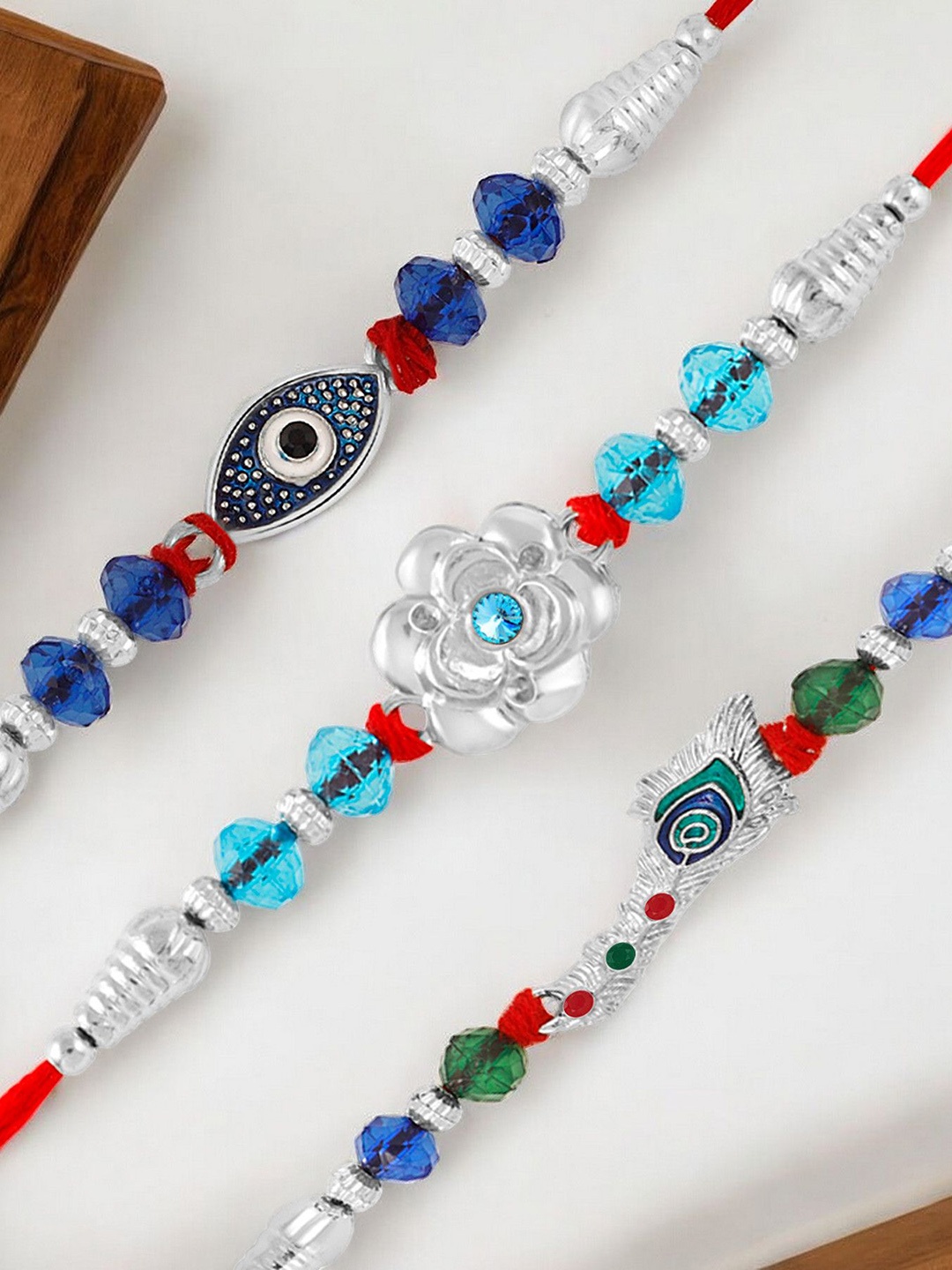 

Okos Set Of 3 Evil Eye Floral Shapes and Feather Thread Rakhis, Silver