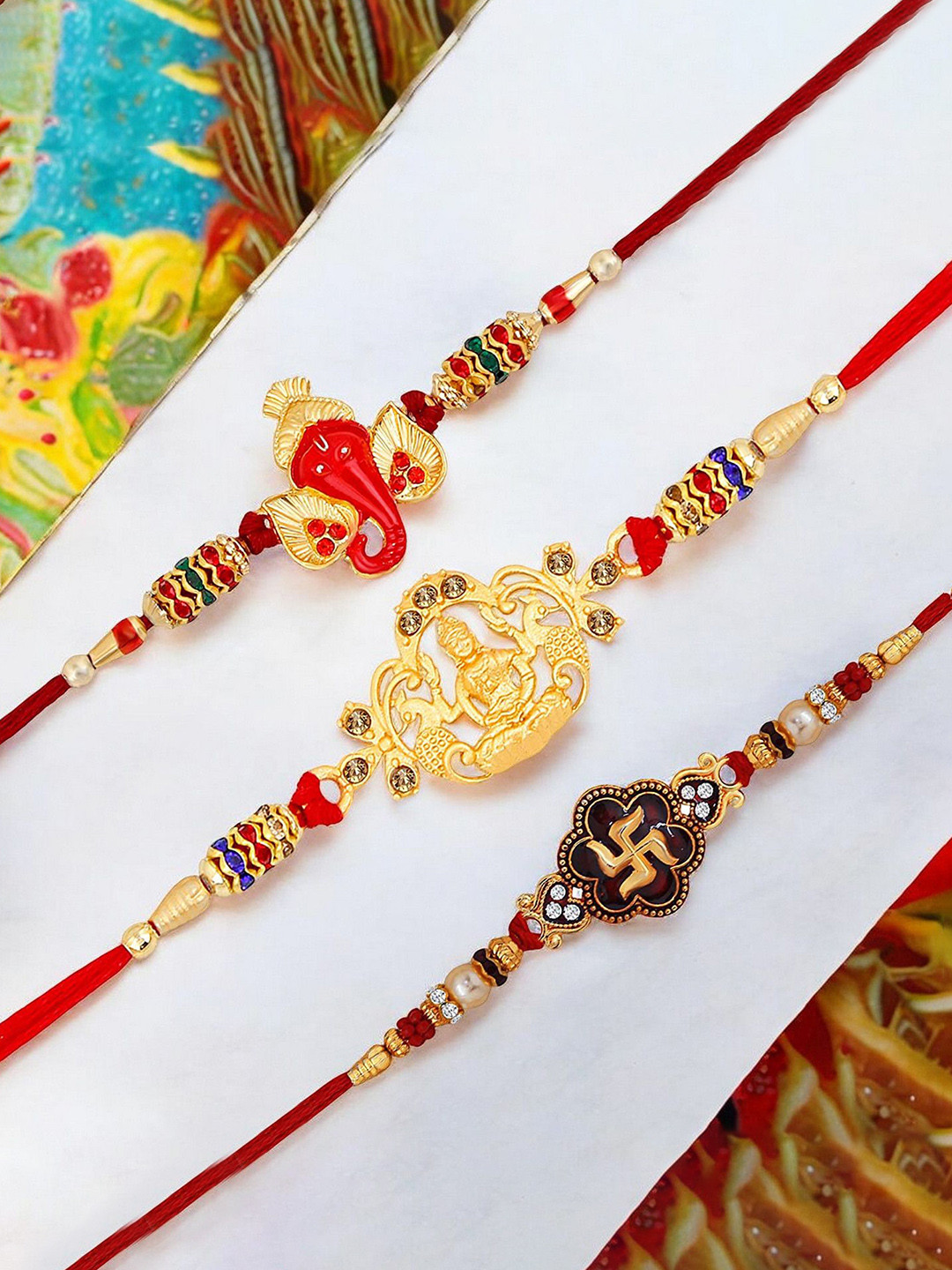 

Okos Set Of 3 Gold Plated Lord Ganesha Laxmi Mata and Swastika Thread Rakhis