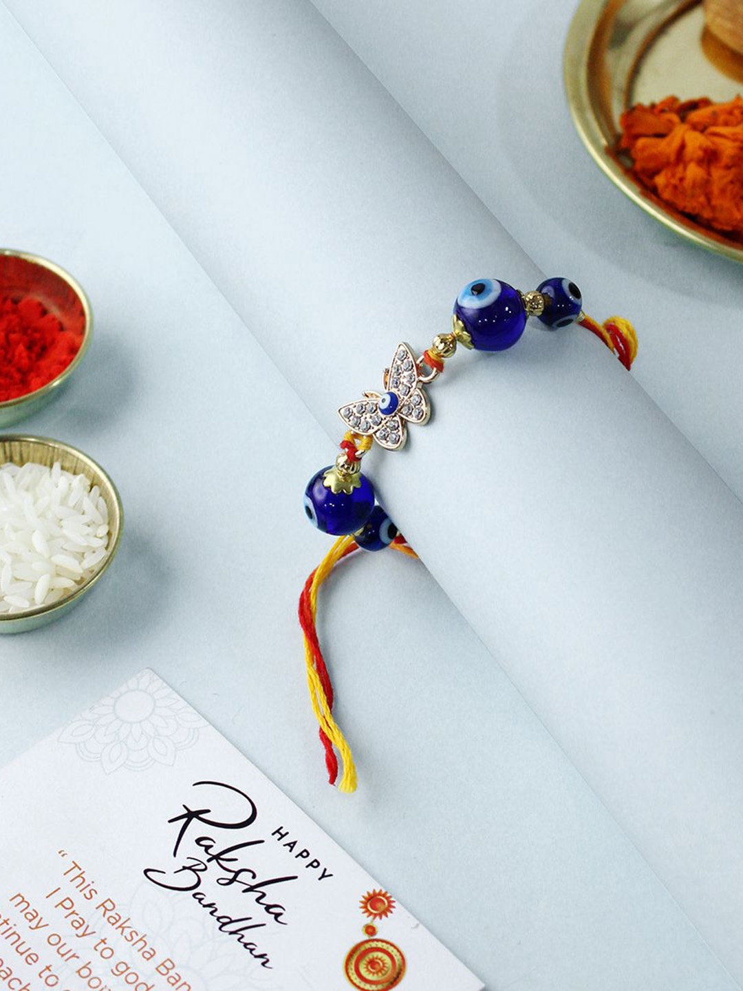 

Shubhanjali Set Of 2 Evil Eye Diamond Butterfly Rakhis With Roli Chawal & Greeting Card, Blue
