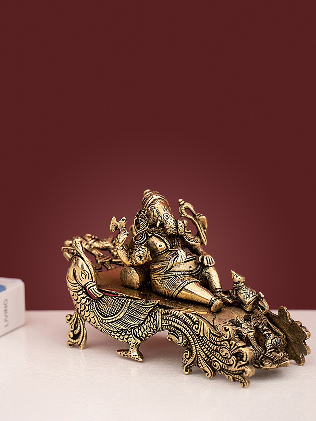 

DecorTwist Gold Toned Textured Ganesha Resting On Peacock Couch Idol Showpiece