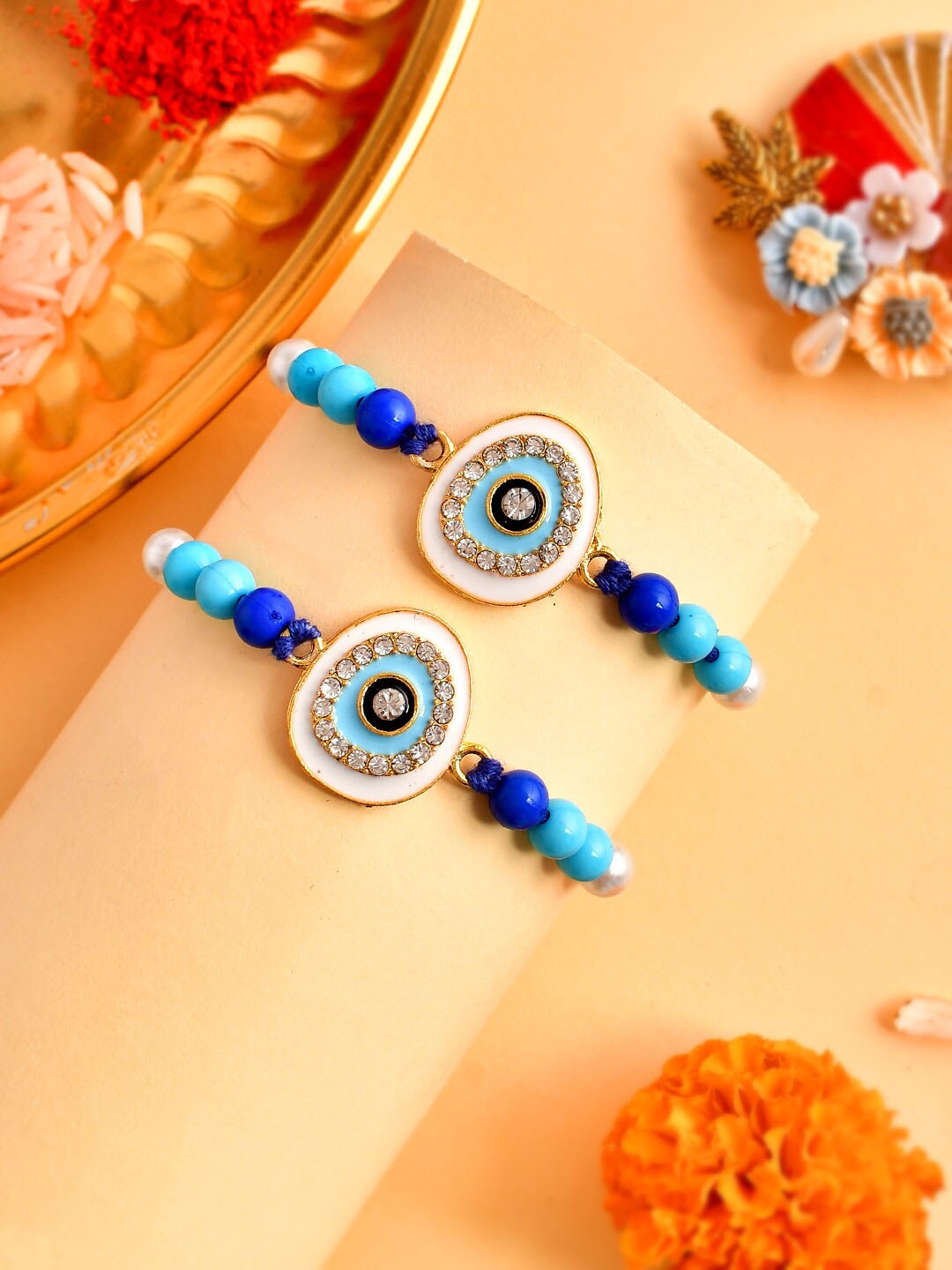 

Aapno Rajasthan Set Of 2 Charm-Studded Thread Rakhi With Roli Chawal & Greeting Card, Blue