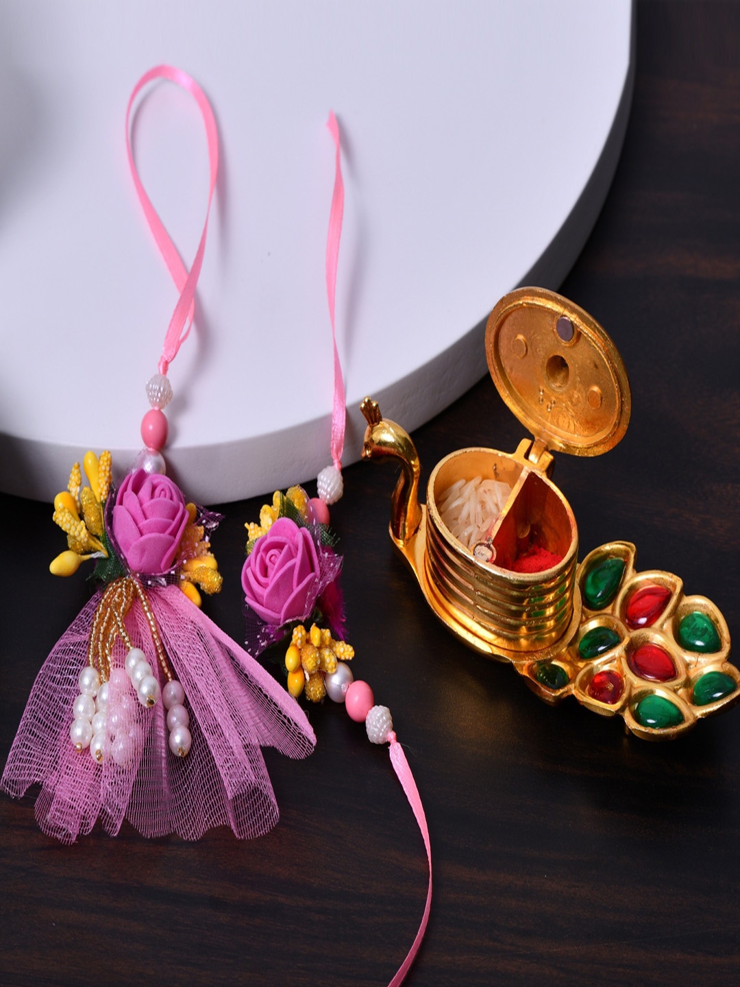 

Fashion Bizz Set Of 2 Charm Rakhi With Roli & Chawal & Peacock Shaped Stand, Pink
