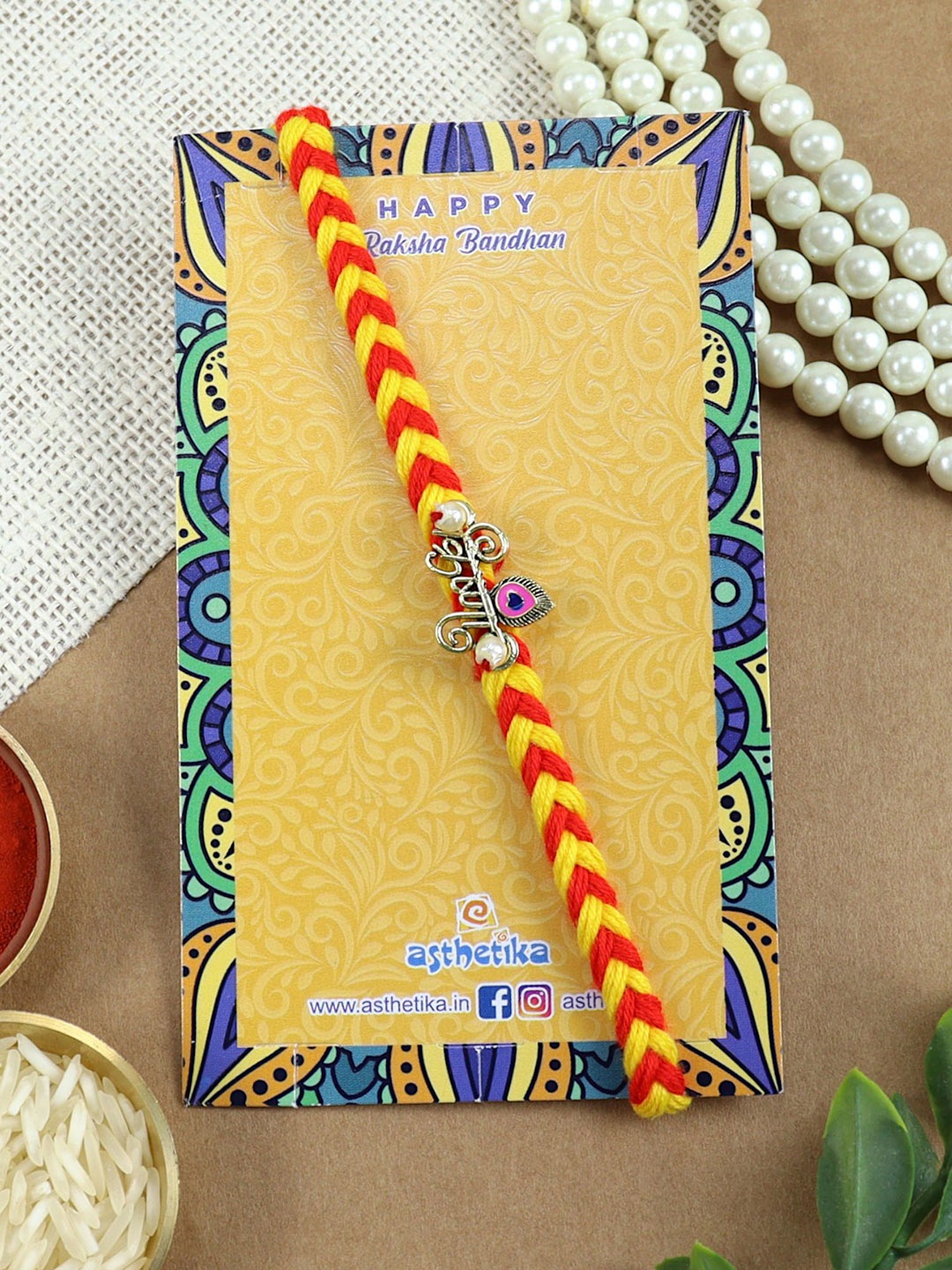 

Asthetika Krishna Charm Braided Rakhi with Roli Chawal, Orange