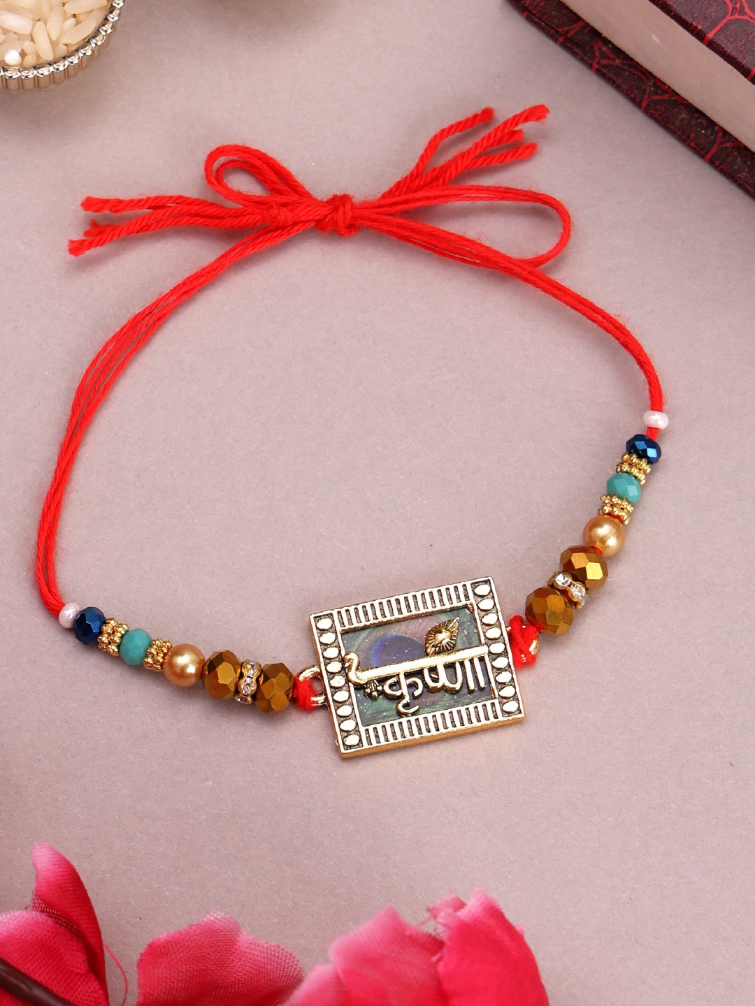 

PANASH Gold-Plated Name Of Krishna Shaped Stone Studded Rakhi With Roli Chawal