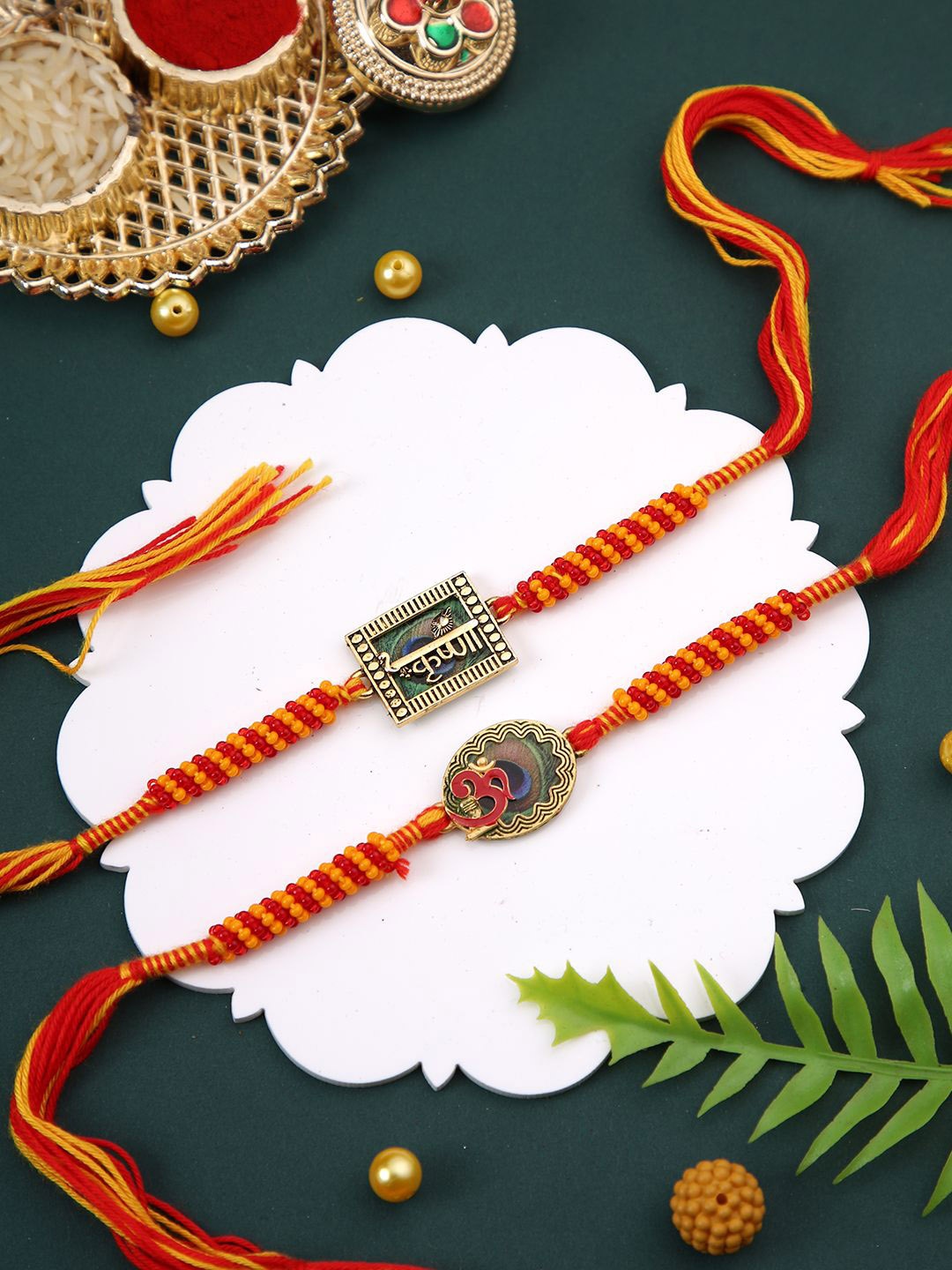 

Aapno Rajasthan Set Of 2 Om & Krishna Enameled Rakhi With Roli Chawal & Greetings Card, Red