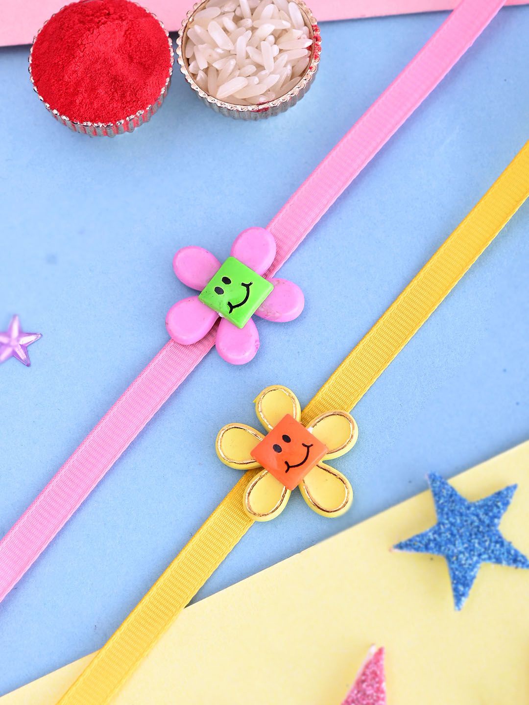 

Aapno Rajasthan Kids Set Of 2 Floral Smiley Thread Rakhis With Roli Rice & Greeting Card, Pink