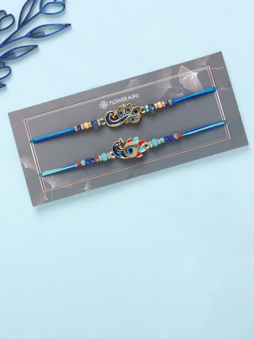 

Floweraura Set Of 2 Beaded Peacock Charm Thread Rakhis With Roli Chawal, Blue