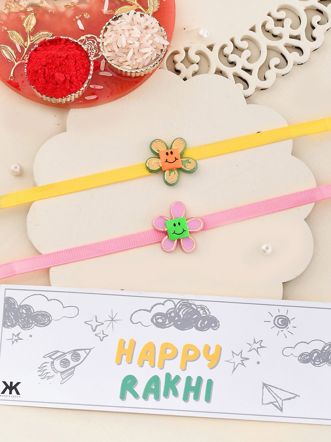 

Kook N Keech Pink and Yellow Smiley Flower Thread Rakhis With Roli Chawal & Greetings Card
