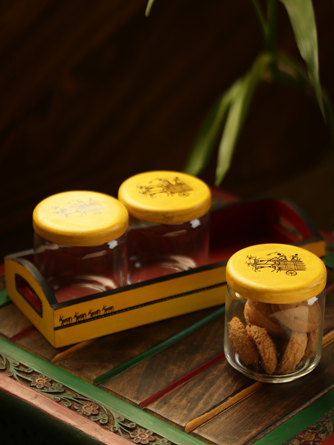 

ExclusiveLane Yellow Tripling Warli Hand-Painted Glass Snacks Jar Set With Wooden Tray, Transparent