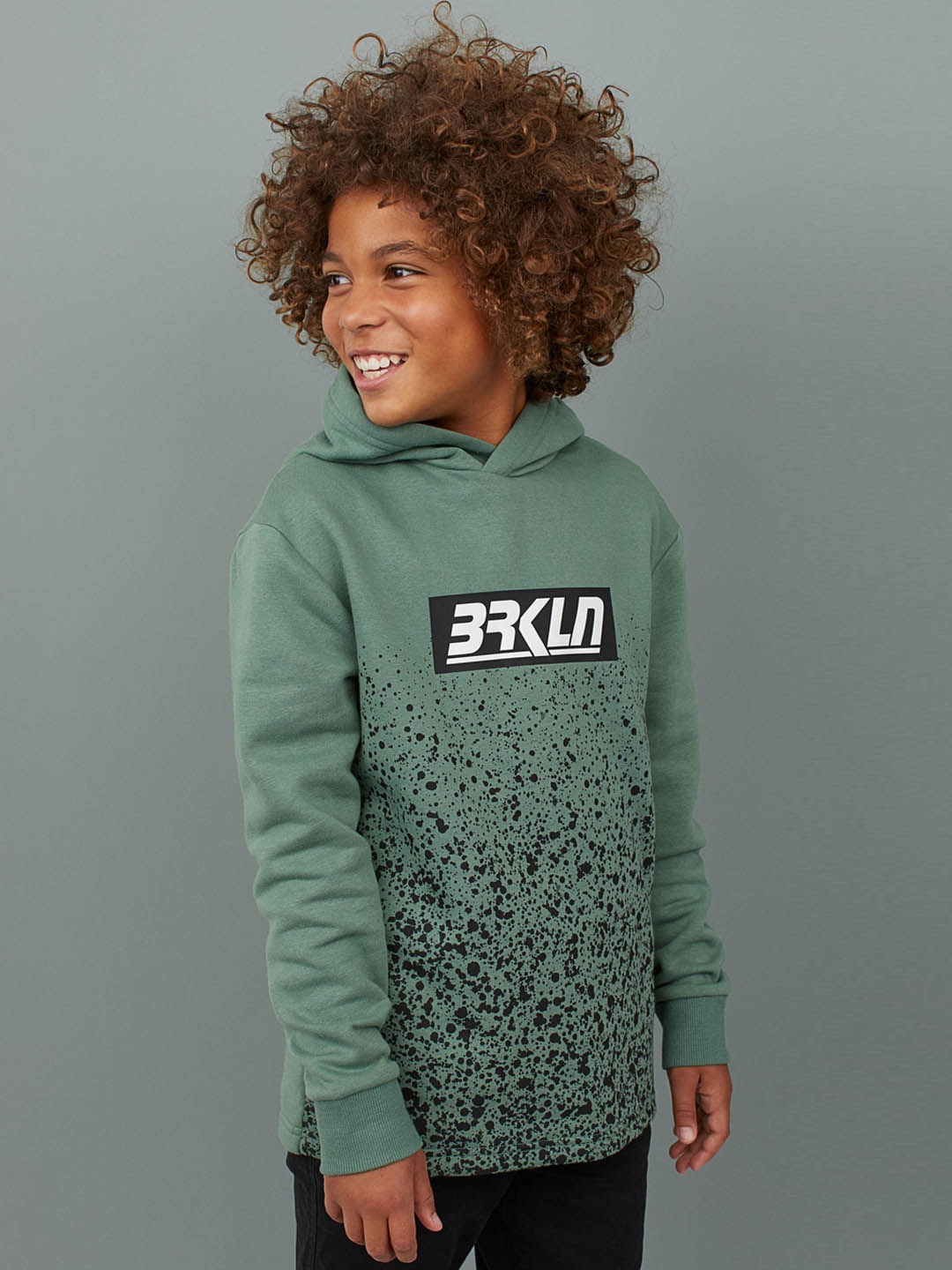 h and m ad. with black kid in green sweatshirt
